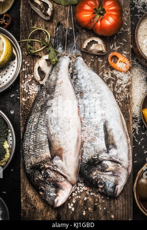 Zwei Rohmaterial dorado Fische auf hölzernen Hintergrund mit Zutaten zum Kochen, Ansicht von oben. Meeresfrüchte Konzept Stockfoto