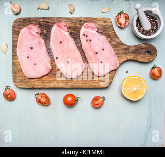 Drei Schweine von rohen Steak auf einem Schneidebrett mit Cherry Tomaten, Zitrone und Messer für Fleisch auf Holz rustikale Hintergrund Top View close up Grenze Platz f Stockfoto