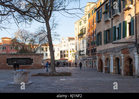 Ponte und Campo de Ghetto Novo bei Sonnenuntergang, Cannaregio, Venice, Italien mit Menschen die Holocaust an der Wand und einem alten Brunnen im Vordergrund ich Stockfoto