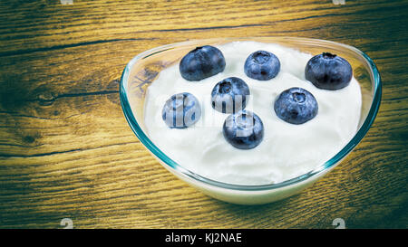 Frische Blaubeeren in fettarmen Joghurt auf einer hölzernen Hintergrund. Frühstück von Joghurt und süße Blaubeeren in einem schönen Glas Schüssel. Stockfoto