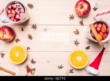 Zwei Tassen mit Kochen Glühwein mit Apfel, Zimt, Nelken und Orangen, Weihnachtsschmuck, gesäumt mit Frame auf einer weißen Holzmöbeln rustikal Hintergrund Stockfoto