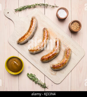 Gegrillte Würstchen liegen auf vintage Schneidbrett mit Rosmarin, Gewürze, Curry Soße und Fleisch Gabel auf einem urigen Hintergrund der Ansicht von oben Stockfoto