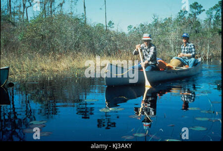 Zwei Männer paddeln mit einem Kanu über ein Gewässer und halten einen Moment der Freizeit und des Transports im Freien fest. Das Foto zeigt die Kanufahrten, bei denen beide Personen in einem traditionellen Kanu durch das Wasser navigieren. Stockfoto