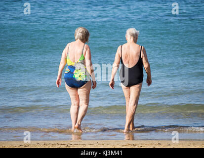 Rückansicht von älteren Frauen, die nach dem täglichen Keep-Fit-Kurs am Strand in Spanien schwimmen gehen Stockfoto