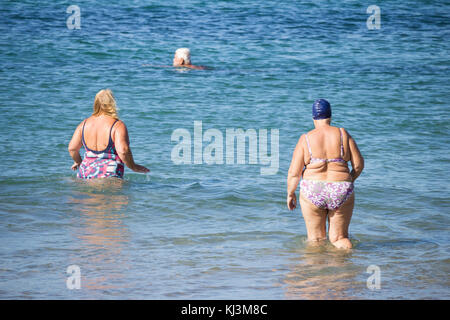 Rückansicht von älteren Frauen, die nach dem täglichen Keep-Fit-Kurs am Strand in Spanien schwimmen gehen Stockfoto