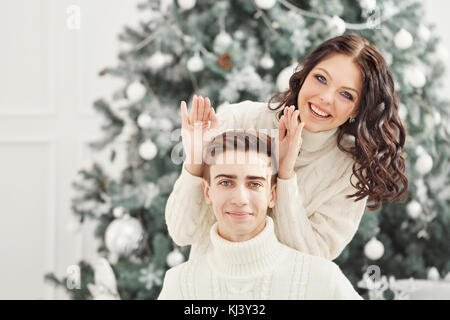 Paar Teenager zu Weihnachten. Sie bunny Ohren Hände zu ihrem Freund macht. Sie täuschen sind. Datum für die Feiertage Stockfoto