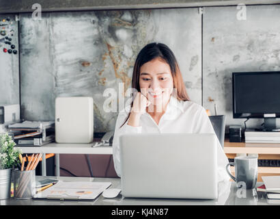 Asien geschäftsfrau am Laptop und lächelndes Gesicht und Rest Kinn, an Hand mit glücklichen Emotion ab gute Nachrichten für geschäftlichen Erfolg im Haus aus Stockfoto