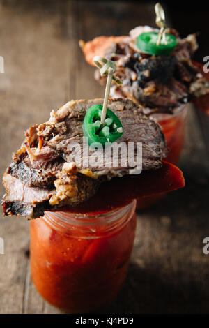 Zwei Gläser mit Bloody Mary cocktail garniert mit BBQ-Fleisch auf rustikalen Hintergrund Stockfoto