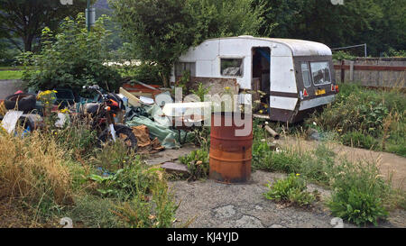 Eine alte verlassene verlassenen Wohnwagen und Motorrad plus andere Bits von Müll auf einem Stück überwucherte Land. Stockfoto