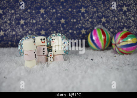 Spaß Weihnachten essen Fotografie Bild mit Marshmallows, der so glücklich Schneemann mit Iced auf Lächeln geformten und Stellung im Schnee mit Farbe Kugeln und Sterne Stockfoto