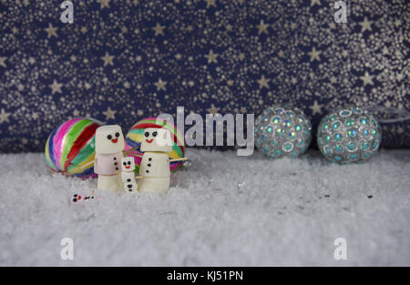 Spaß Weihnachten essen Fotografie Bild mit Marshmallows, der so glücklich Schneemann mit Iced auf Lächeln geformten und Stellung im Schnee mit Farbe Kugeln und Sterne Stockfoto