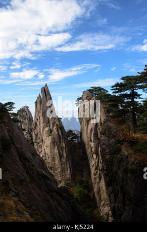 Scharfer Punkt Granitblock mit Gipfeln im Hintergrund mit blauem Himmel und weißen Wolken am Gelben Berg in China Stockfoto