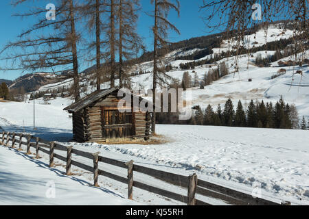 Kleine Holzhütte und Zaun unter Bäume im Winter Tag mit frischem Schnee in den Bergen. Stockfoto