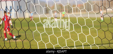 Fußball-Spiel in der Arena durch Fußball-Netze. Verschwommen Spieler Hintergrund. Stockfoto