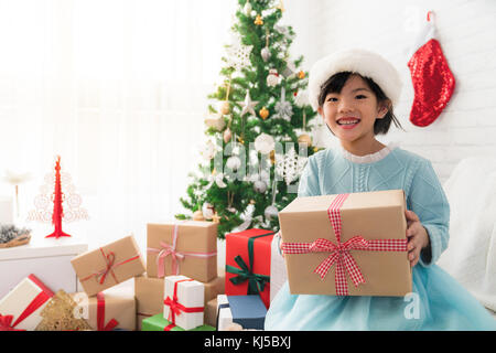 Happy little cute Asian Girl Holding a Christmas Gift box Sitzen auf einem Sofa in der Dekoration Wohnzimmer. Stockfoto