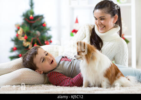 Portrait eines glücklichen Mutter und ihren kleinen Sohn mit Hund verbringen zusammen Weihnachten zu Hause in der Nähe der x-mas Tree Stockfoto