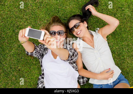 Weibliche beste Freunde, die auf dem Gras und selfies Stockfoto