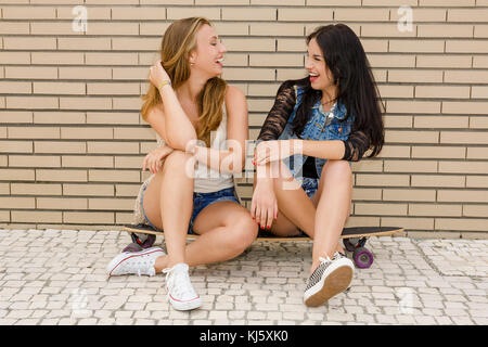 Zwei schöne und junge Freundinnen Spaß mit einem Skateboard, vor einer Mauer Stockfoto