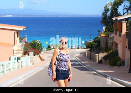 Eine touristische Frau posiert für ein Foto mit dem Blick auf Spiaggia di di Strand Rena Bianca von der Stadt Santa Teresa di Gallura. Stockfoto