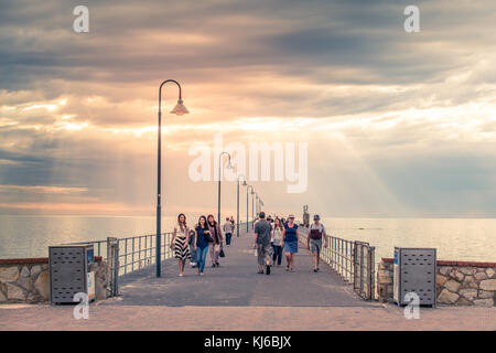 Adelaide, Australien - 19. Januar 2016: Die Menschen laufen am Glenelg Jetty bei Sonnenuntergang. Der Steg wurde am 25. April 1859 für die Öffentlichkeit eröffnet und ist einer der beliebtesten Stockfoto