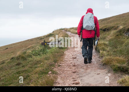 Mann, der bei Wind und Regen auf dem Old man of Hoy-Fußweg am Schild gefährliche Klippen vorbeiläuft, Hoy, Orkney, Schottland, Großbritannien Stockfoto