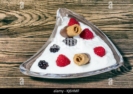 Süße Versuchung mit frischem Obst und Gebäck. Glas Schale mit Joghurt, Himbeeren und Brombeeren auf Holz- Hintergrund. Stockfoto