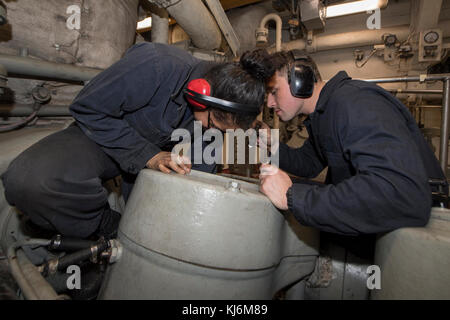 BETRIEBSBEREICH DER 5. US-FLOTTE (NOV 13, 2017) Engineman 2. Klasse Nellisha Gonzales (links), gebürtig aus Los Angeles, Und Engineman 2nd Class Brendan MacDonald, ein gebürtiger Boston, die beide an die Engineering-Abteilung an Bord des Amphibiendocks Landungsschiff USS Pearl Harbor (LSD 52), führen routinemäßige Wartung an einem Hauptmotor im Hauptraum des Schiffes. Pearl Harbor wird in der 5. US-Flotte Einsatzgebiet zur Unterstützung von maritimen Sicherheitsoperationen entwickelt, um Verbündete und Partner zu beruhigen, und die Freiheit der Schifffahrt und den freien Fluss von com zu erhalten Stockfoto