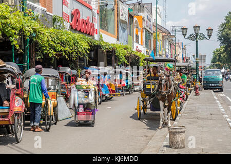 Zyklus Rikschas/becak und Pferdekutschen für den öffentlichen Verkehr in der Jalan Malioboro, wichtigsten Einkaufsstraße in Yogyakarta, Java, Indonesien