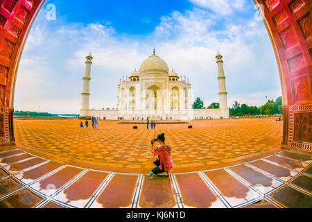 Agra, Indien - 20. September 2017: nicht identifizierte Frau im Boden sitzen und genießen die schöne Aussicht auf das Taj Mahal durch eine große Tür, ist ein Elfenbein - weißer Marmor mausoleum am südlichen Ufer des Yamuna Flusses in der indischen Stadt Agra, Uttar Pradesh, Fischaugen-Effekt Stockfoto