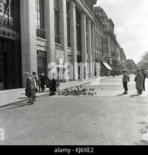 1953, historische, 52-60 Avenue Champs-Elysees, eine Dame speist die Tauben außerhalb des Art déco-Gebäude, wo der Film, "The Happy Time" mit den berühmten Schauspieler Charles Boyer erschien im Kino Monte-Carlo. Dieses Einzelzimmer - Zimmer Kino war einer von vielen, die auf diesem Weg zu dieser Zeit befanden, einschließlich der Bryon und den Broadway. Stockfoto
