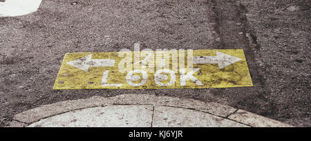 Gelb-ish und graphischen Zeichen auf dem Asphalt Fußgänger zu warnen, rechts und links vor dem Überqueren der Straße. Stockfoto