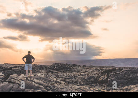Ein Mann auf der Suche über die Lavafelder in Volcanoes National Park in Hawaii bei Sonnenuntergang Stockfoto
