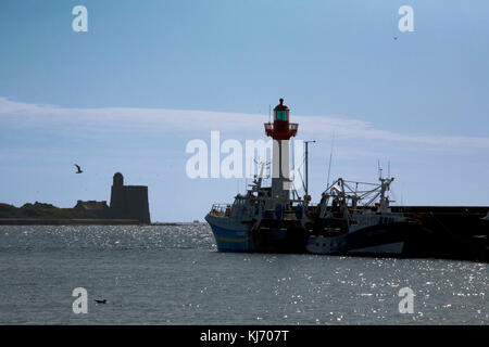 Eingang zum Hafen von St Vaast: Vauban-Turm auf der Insel Tatihou und verankerte Fischerboote und Leuchtturm auf der Wellenbrecher, Normandie, Frankreich Stockfoto