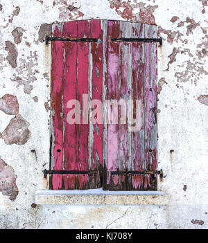 Close-up of an old window with closed red worn wooden shutters on a white decrepit wall in winter. Stockfoto