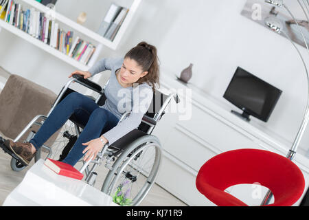 behinderte Frau versuchen, Buch Rollstuhl im Wohnzimmer Stockfoto