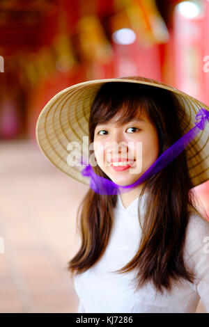 Vietnam, Hue, Forbidden Purple City. Junge Vietnamesin in einem Tempel, die ein traditionelles Ao Dai Kleid und einen nicht-La-asiatischen konischen Hut trägt Stockfoto
