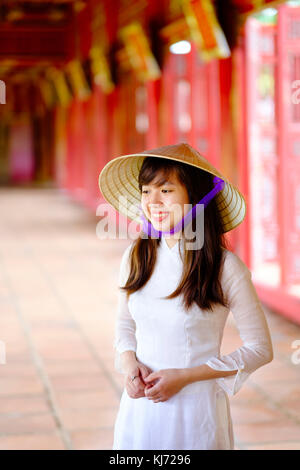 Vietnam, Hue, Forbidden Purple City. Junge Vietnamesin in einem Tempel, die ein traditionelles Ao Dai Kleid und einen nicht-La-asiatischen konischen Hut trägt Stockfoto