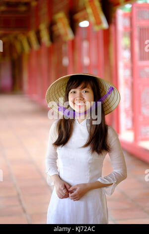 Vietnam, Hue, Forbidden Purple City. Junge Vietnamesin in einem Tempel, die ein traditionelles Ao Dai Kleid und einen nicht-La-asiatischen konischen Hut trägt Stockfoto