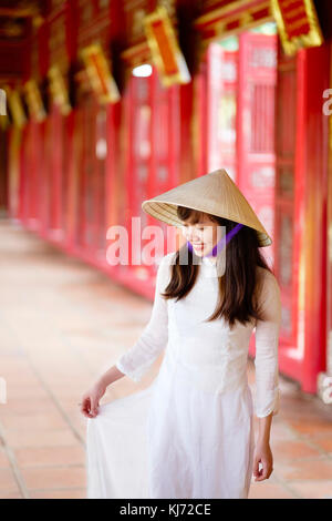 Vietnam, Hue, Forbidden Purple City. Junge Vietnamesin in einem Tempel, die ein traditionelles Ao Dai Kleid und einen nicht-La-asiatischen konischen Hut trägt Stockfoto