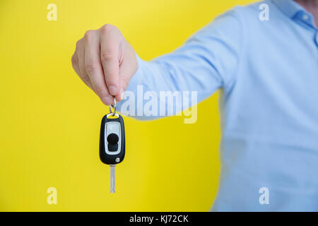 Nahaufnahme Foto der männlichen Hand mit einem autoschlüssel. Person trägt ein blaues Hemd, stand vor der hellen gelben Hintergrund Stockfoto