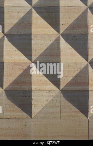 Die geometrisch gemusterte Betonwand hat Diamantformen, die mit Schatten des Sonnenlichts am Nachmittag akzentuiert sind Stockfoto