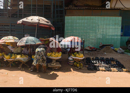 . Mehrere kleine Stände mit Obst und Gemüse Menschen saßen im Schatten der Sonnenschirme an der Seite der Straße, Uganda, Afrika Stockfoto