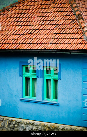 Land Side House lebhafte helle blaue Farbe Wand mit zwei grünen Fenster und Dach, Country Side House Stockfoto