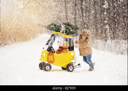 Eine schöne, vier Jahre alten Jungen tragen Schaffellmantel spielen auf verschneiten, Winter Forest Road Stockfoto