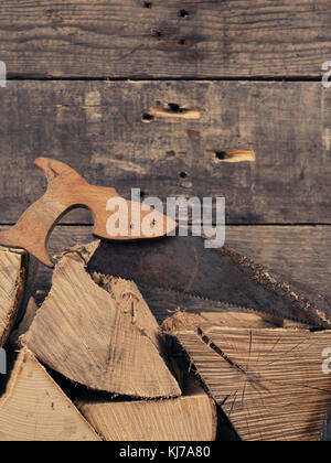 Stapel von Brennholz mit einem alten, rostigen Säge, Platz für Text auf Holz Wand Stockfoto