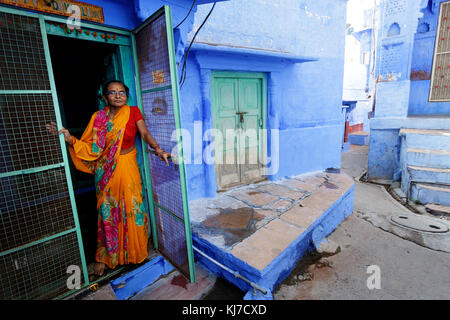 Alte indische Frau in traditioneller Kleidung öffnen Die grüne Eingangstür gekleidet, Jodhpur, Indien. Stockfoto