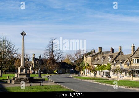 War Memorial steinernes Kreuz auf Cotswolds Village Green von Cotswold stone Geschäfte übersehen. High Street, Broadway, Worcestershire, England, Großbritannien, Großbritannien Stockfoto