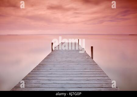Blick auf malerische Meereslandschaft mit hölzernen Pier bei Sonnenuntergang rot und orange Farben Stockfoto
