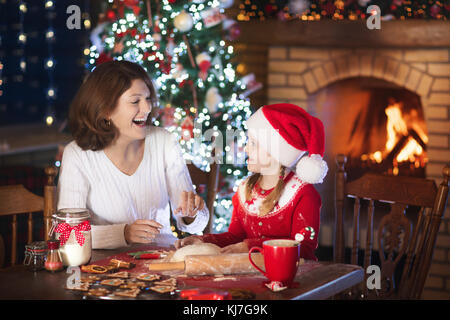 Mutter und Tochter backen Weihnachtsplätzchen am Kamin und geschmückten Baum. Mutter und Kind backen Weihnachten Süßigkeiten. Familien mit Kindern feiern Weihnachten Stockfoto