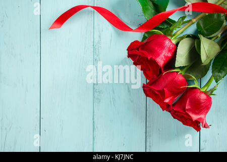 Rote Rosen mit einem roten Band auf einem aquamarin Holzbrett. Valentinstag oder Geburtstag Hintergrund Stockfoto